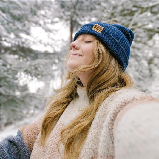 Woman wearing a blue Keep Tahoe Blue beanie in a snowy forest