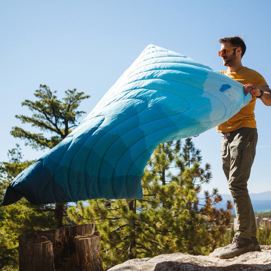 Camper shakes out Sierra Nevada puffy blanket from Rumpl for Keep Tahoe Blue in the woods